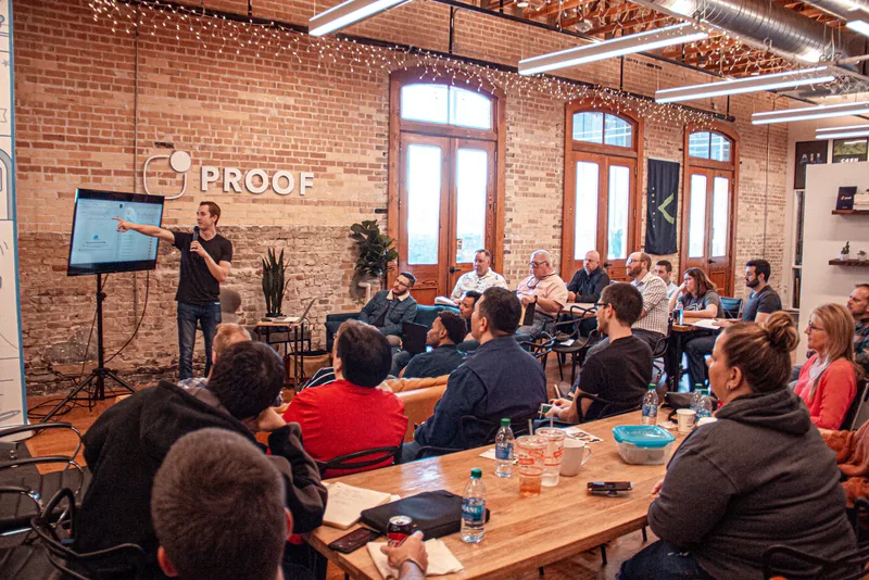 A man presenting to a group of people in a brick-walled office workspace